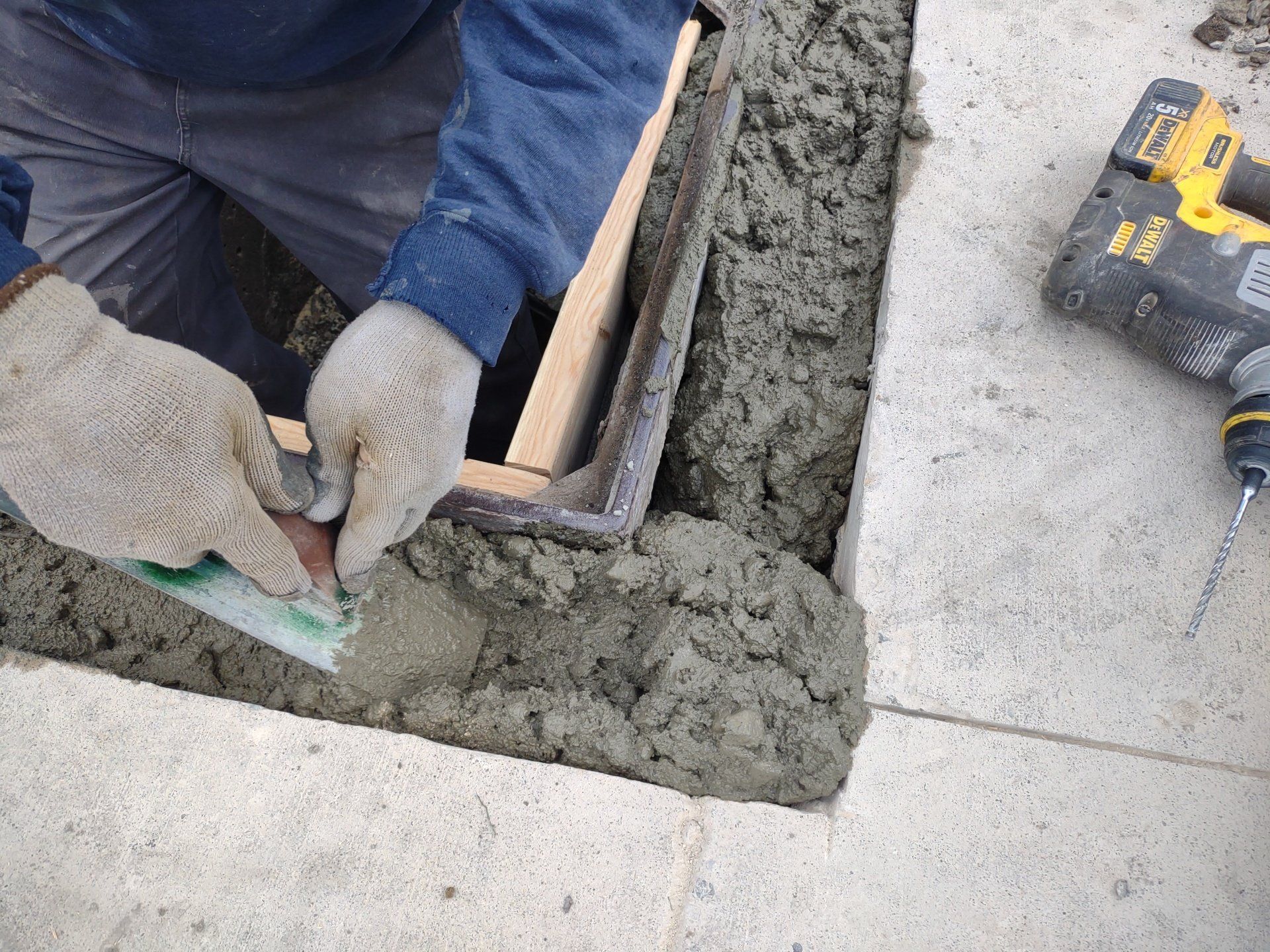 A masonry forming wet cement around a wooden frame set in concrete blocks; drill is nearby.