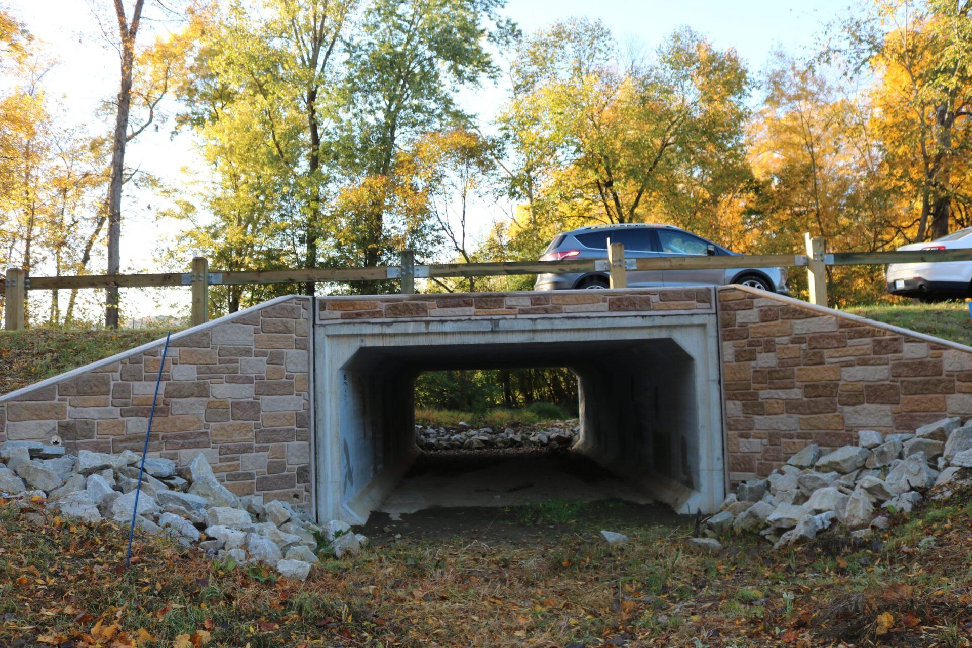 Stone-faced tunnel under a road, with vehicles visible on top and trees in the background.