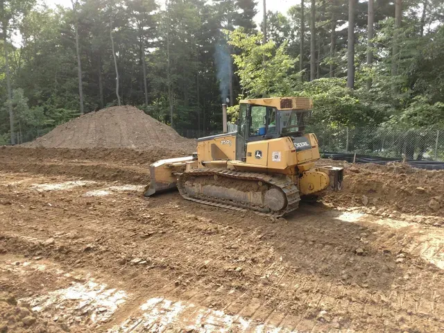 Yellow bulldozer on muddy ground, clearing earth near a pile of dirt and forest.