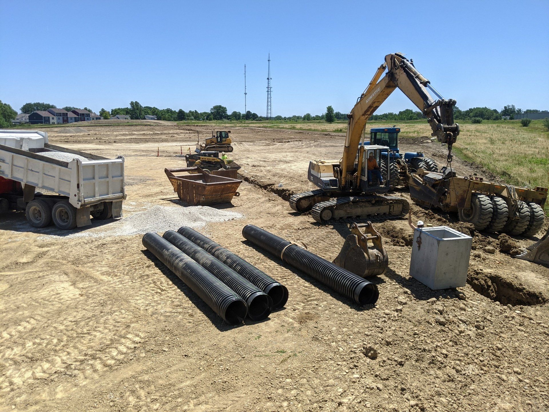 Construction site with excavator, pipes, and dump truck under a clear sky.