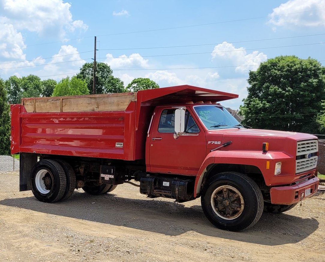 Red dump truck parked outdoors on gravel.