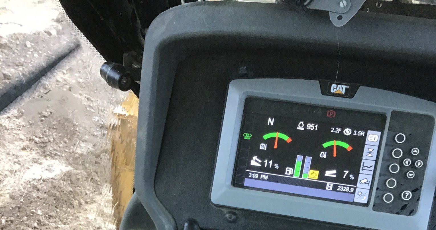 Dashboard of a Caterpillar machine showing gauges and a screen, outdoors.