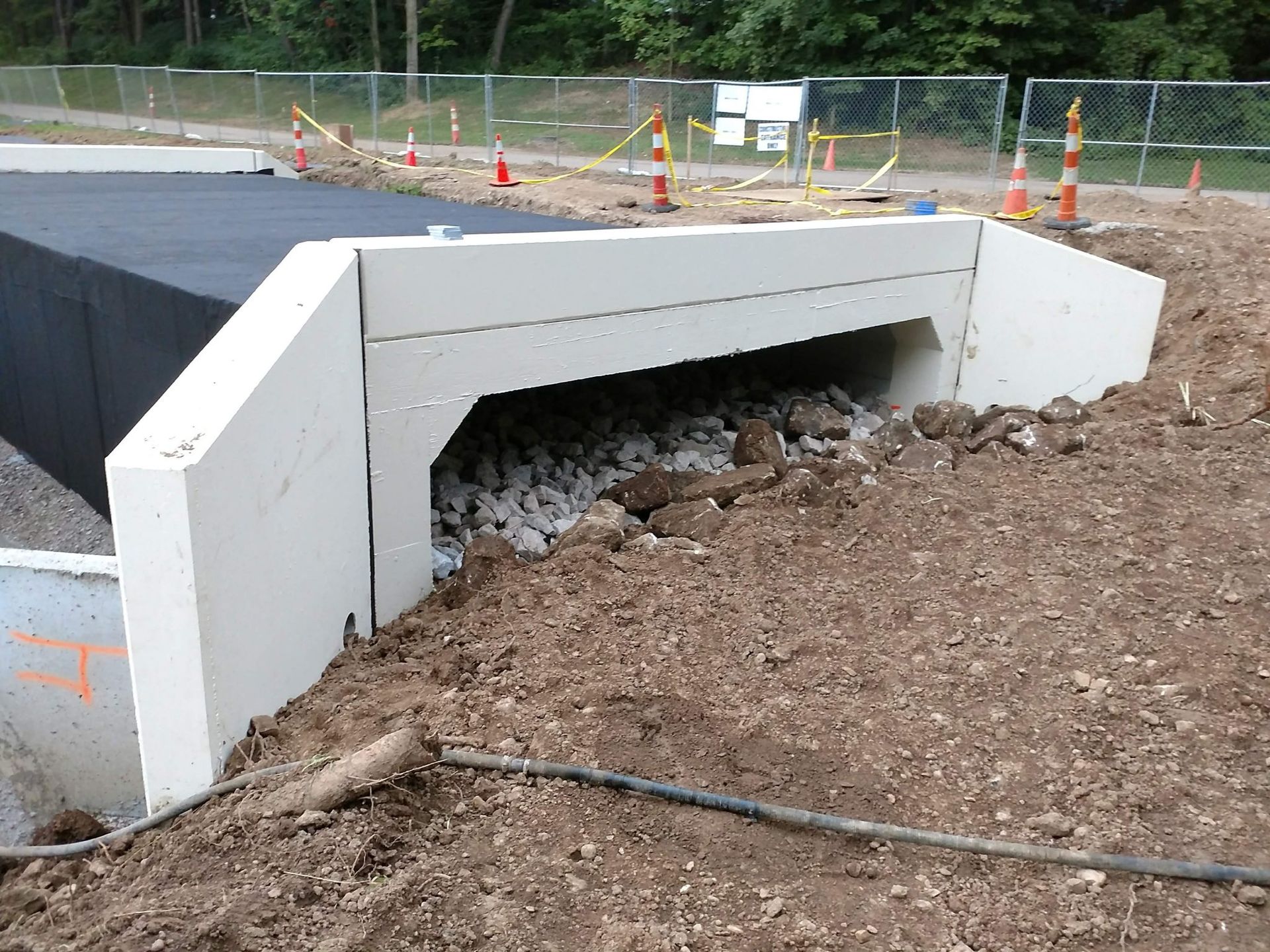 Concrete box culvert under construction, dirt around opening, black top above.