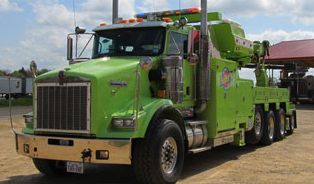 Green heavy-duty tow truck parked outdoors on a dirt lot