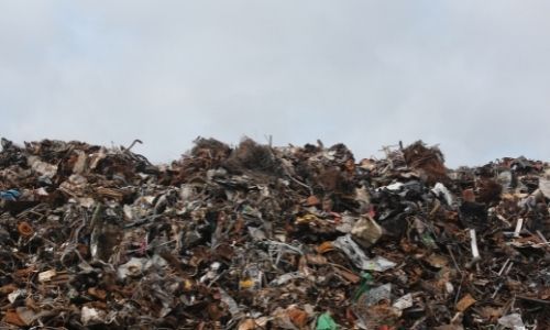 Large heap of mixed trash and debris piled against a cloudy sky.