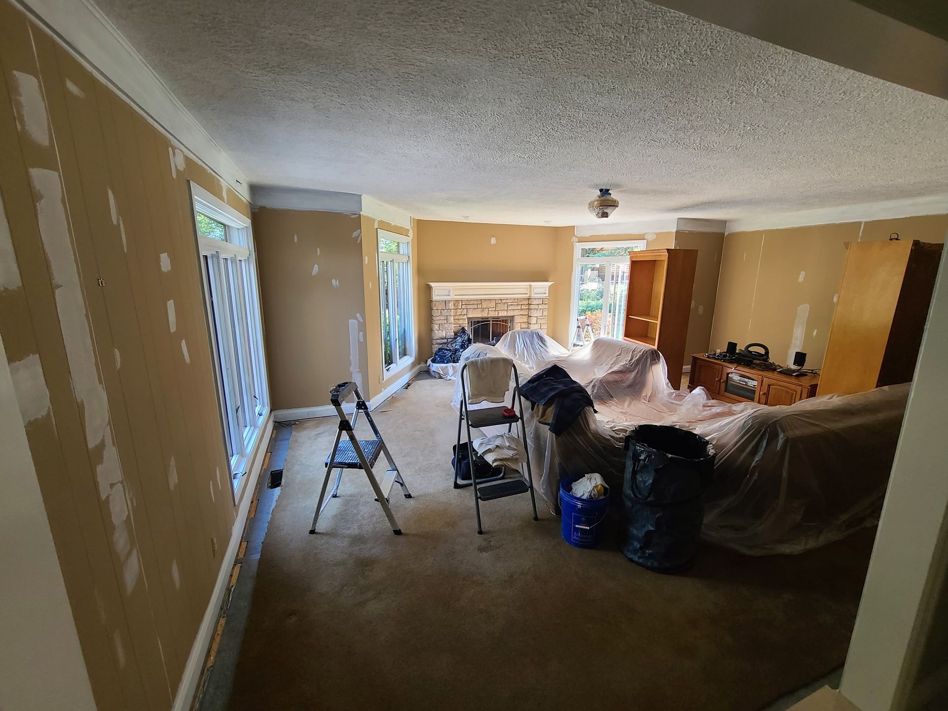 A living room with a couch , chairs , and a fireplace covered in plastic.