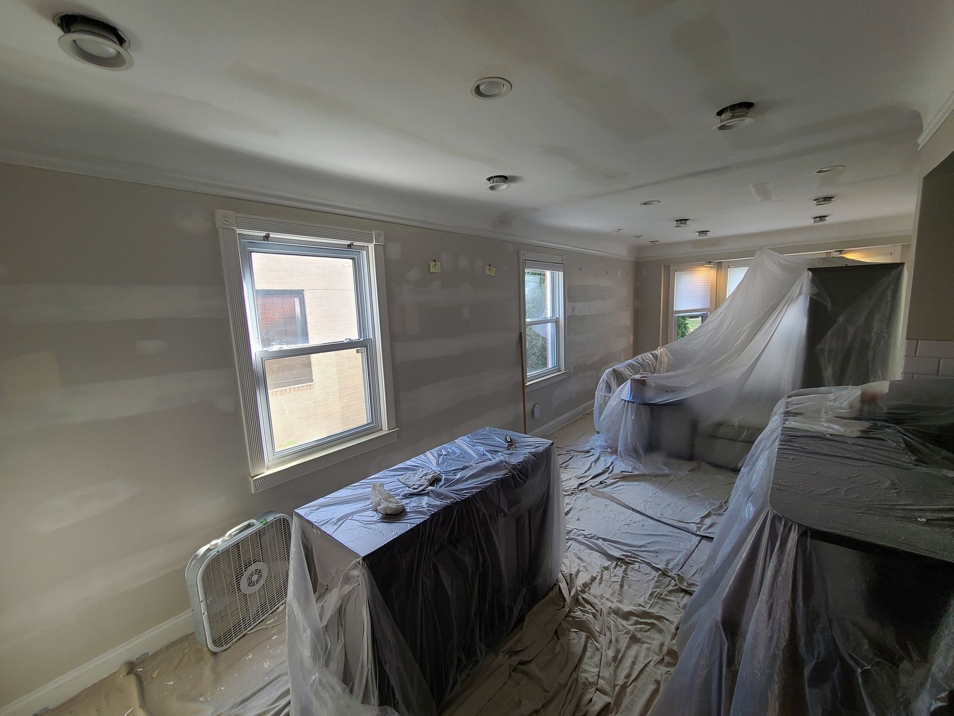 A room with a table and two windows covered in plastic.