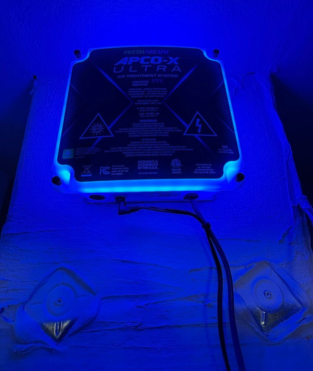 Blue-lit wall-mounted control box with warning labels and wires hanging below.