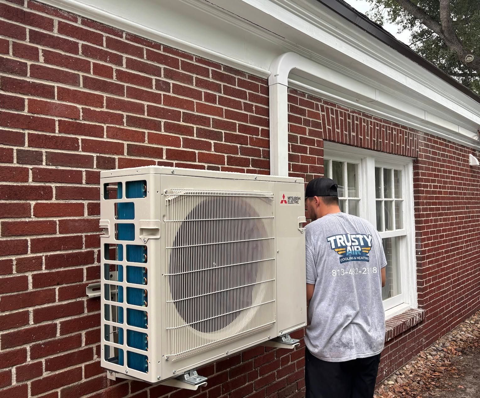 Technician installing a wall-mounted outdoor air conditioner on a brick house exterior
