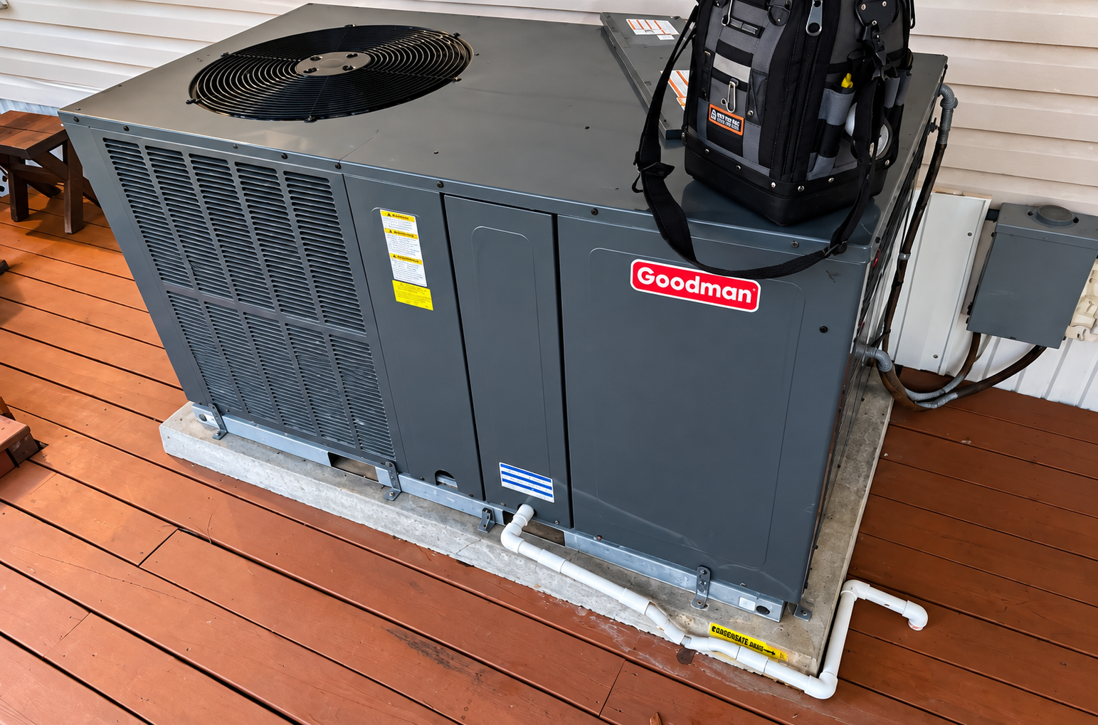 Gray Goodman HVAC unit on a wooden deck beside a wall, with a fan and controls visible.