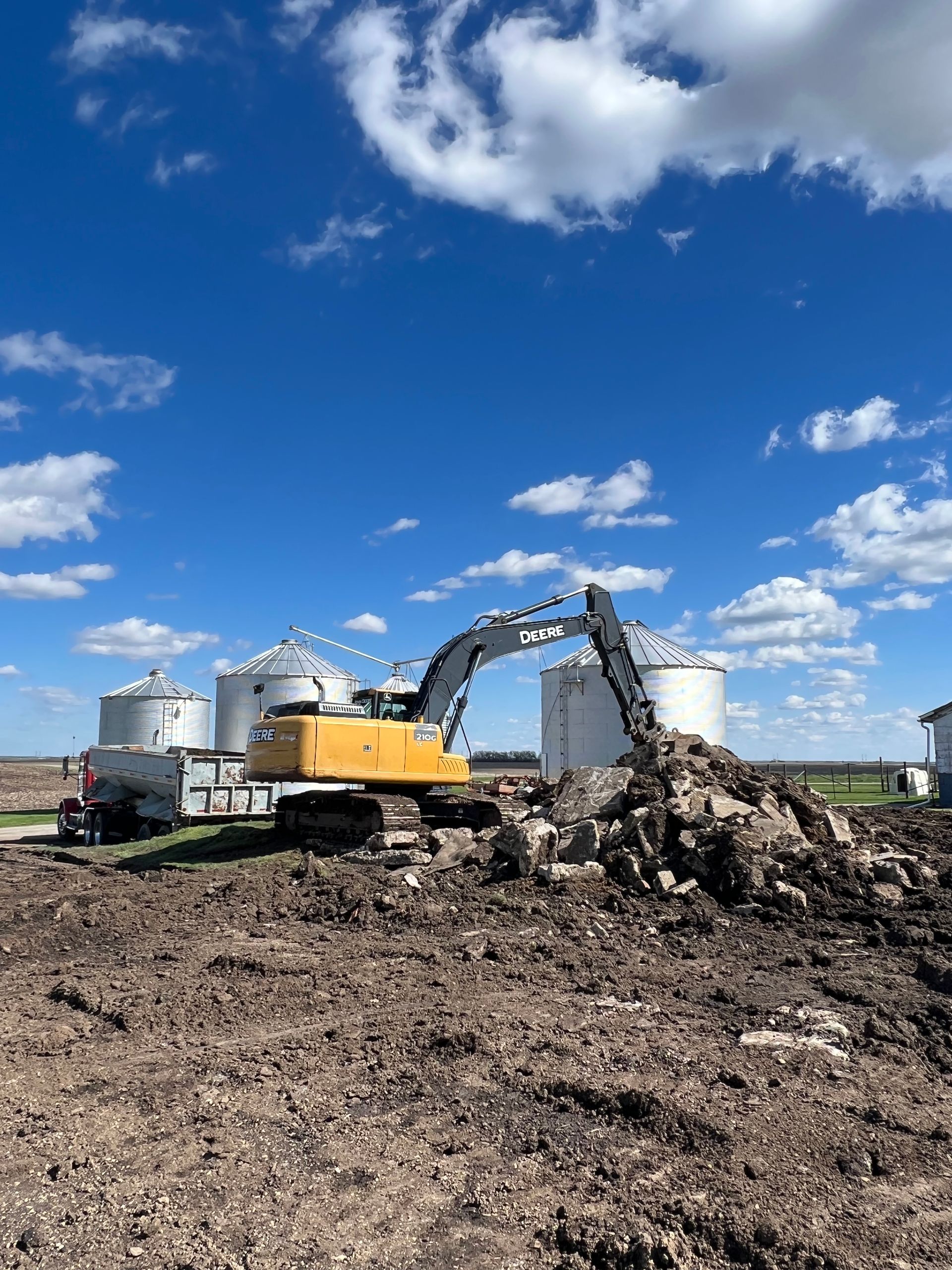A large yellow excavator is digging a large pile of dirt in a field.