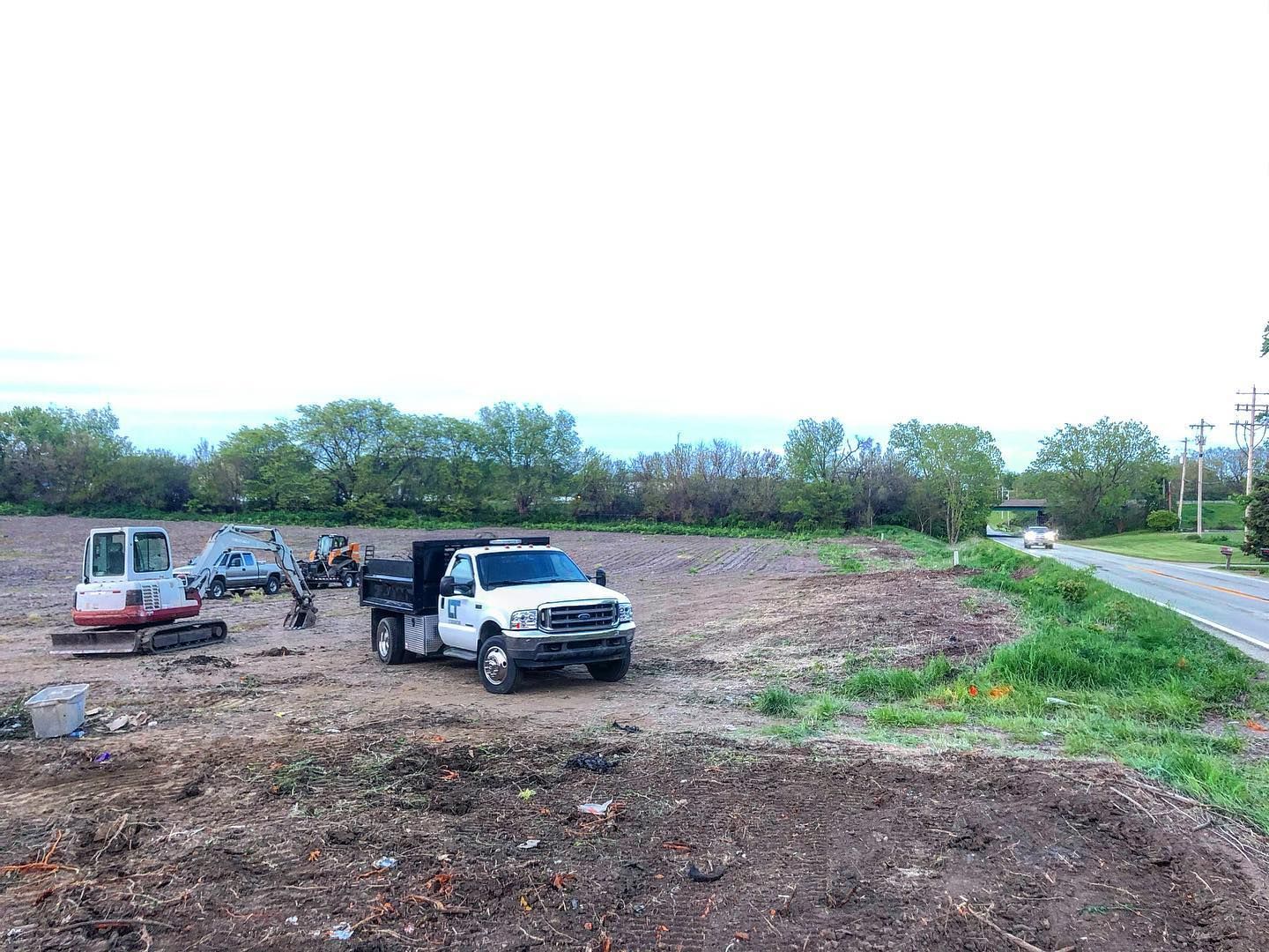 A white truck is parked in a dirt field next to a road.