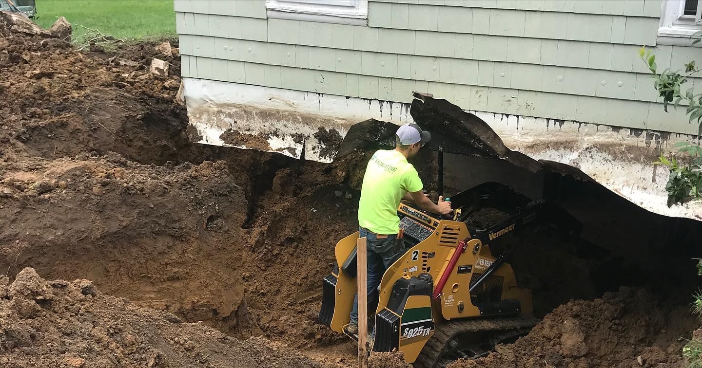 A man is using a bulldozer to dig a hole in front of a house.