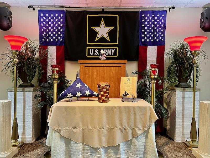 A memorial setup with an American flag, Army insignia, and a draped table.