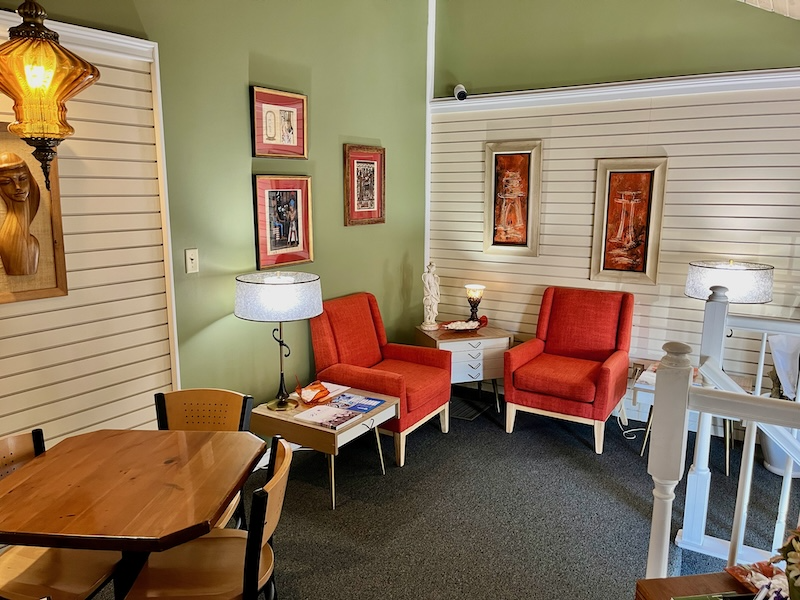 Cozy seating area with orange chairs, artwork, small table, and a wooden dining table.