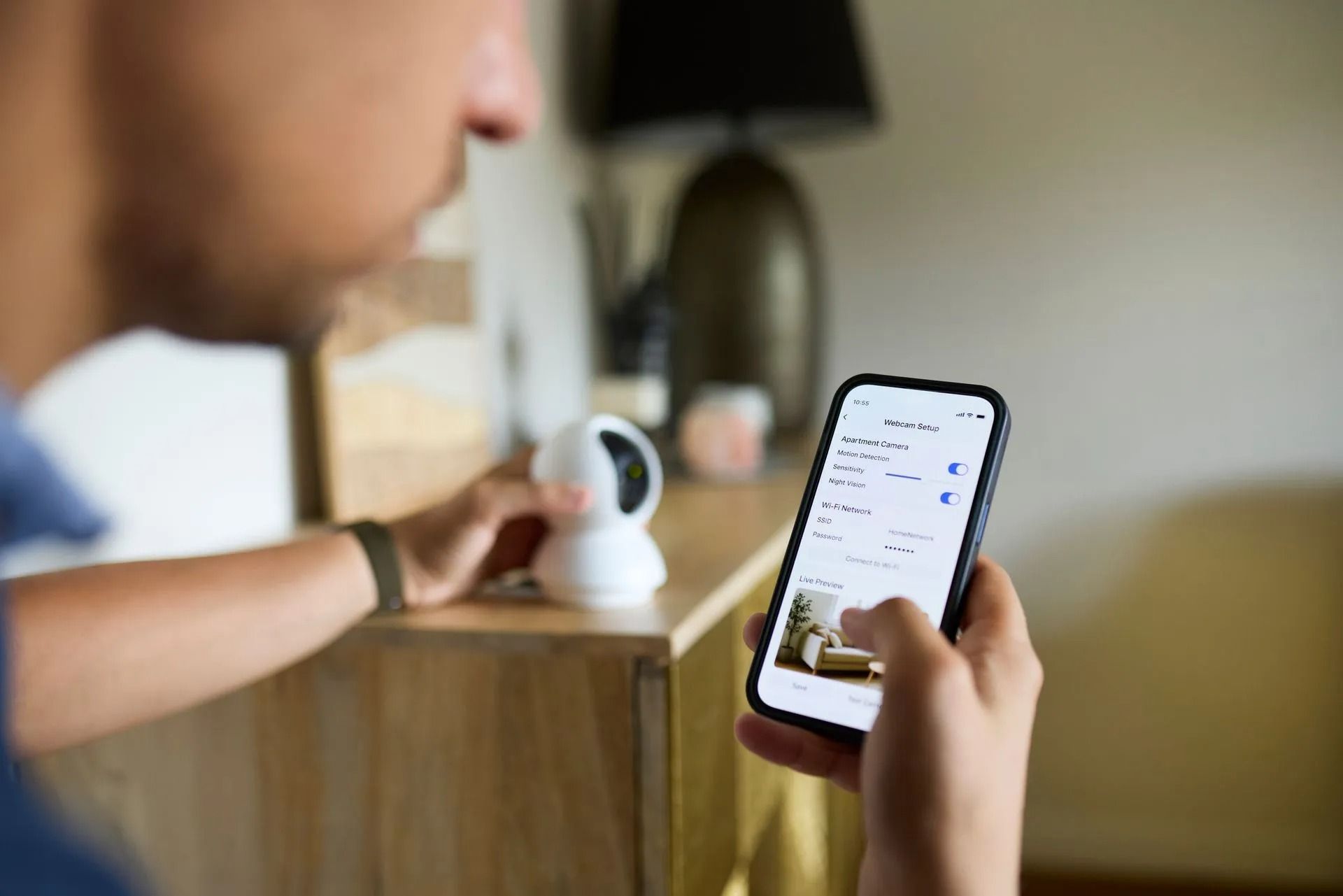 Person holding phone, interacting with security camera app, camera on a shelf.