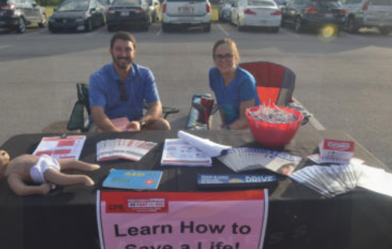 Two people at a table with CPR training materials and a baby doll; 