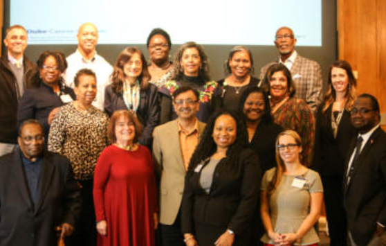 Group of diverse people posing for a photo, indoors. Some smiling, formal attire.