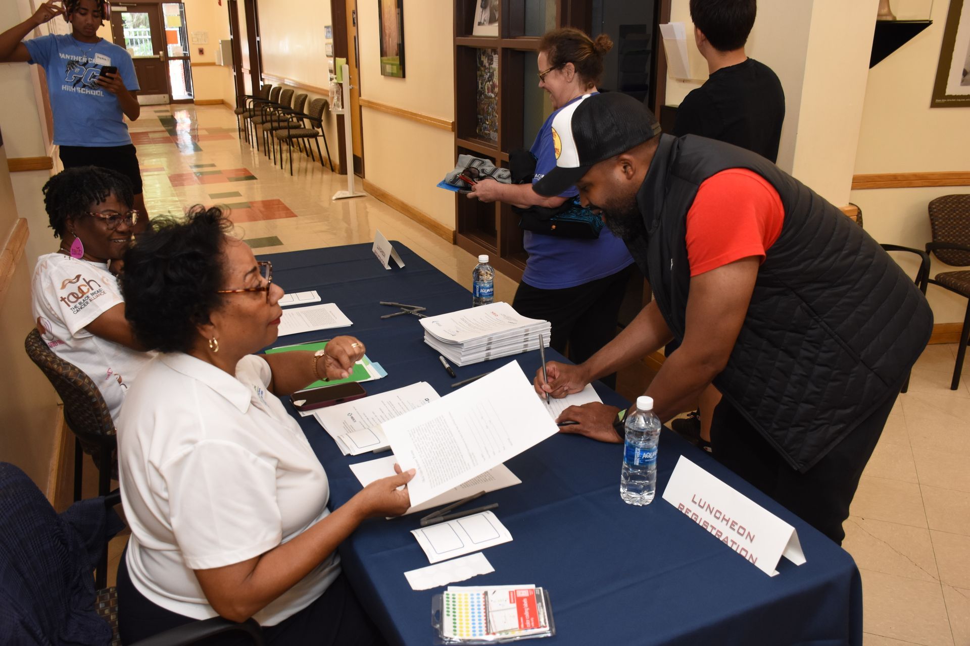 People registering at a table, some reviewing forms. Indoor setting, a water bottle present.