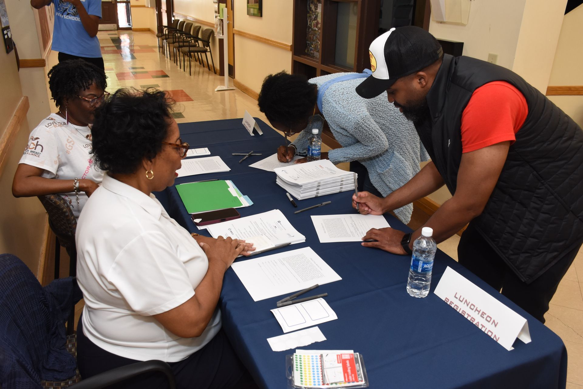 People signing documents at a table. Papers and a water bottle are visible.