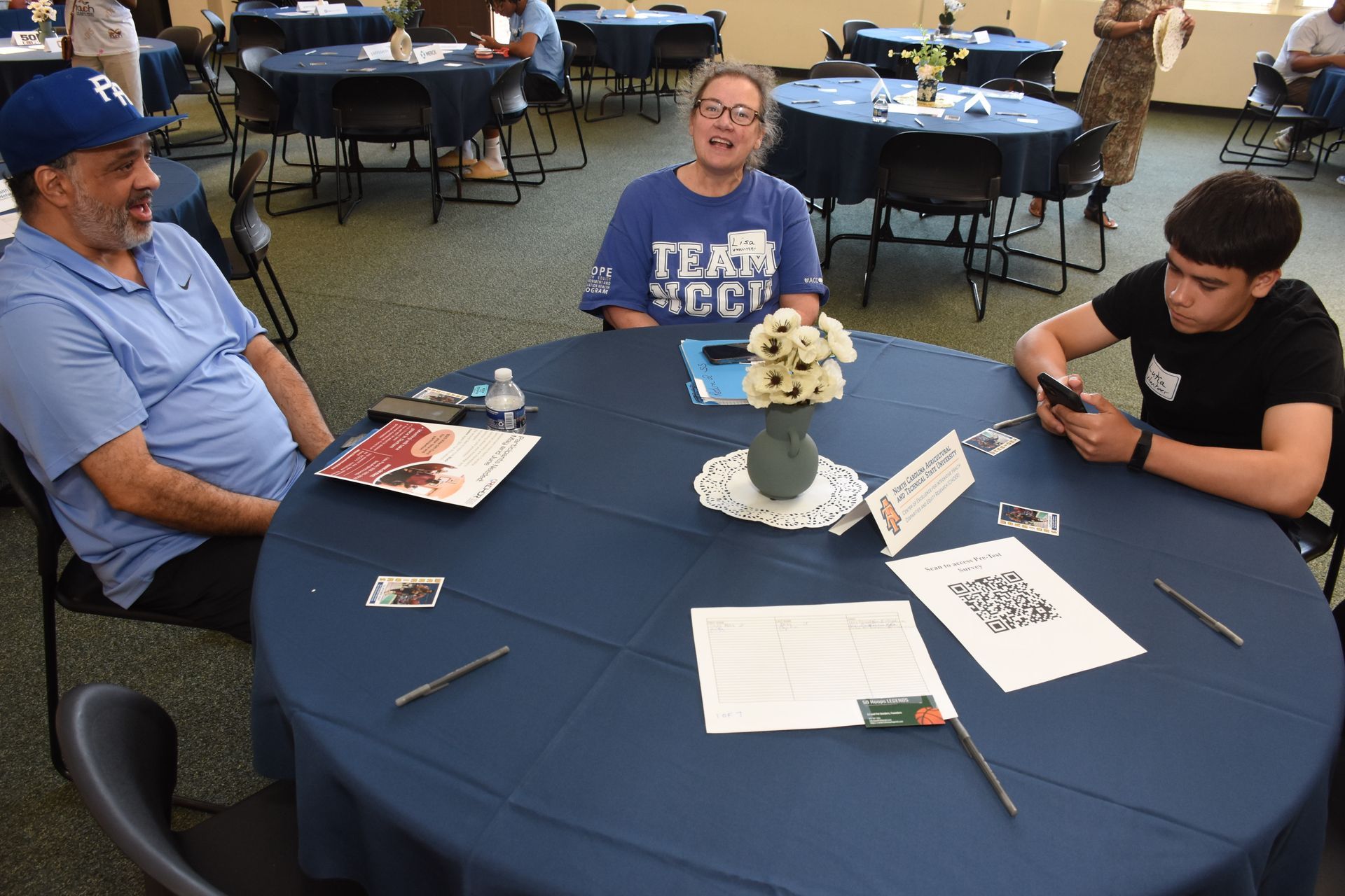 Three people seated at a round table covered in a blue cloth