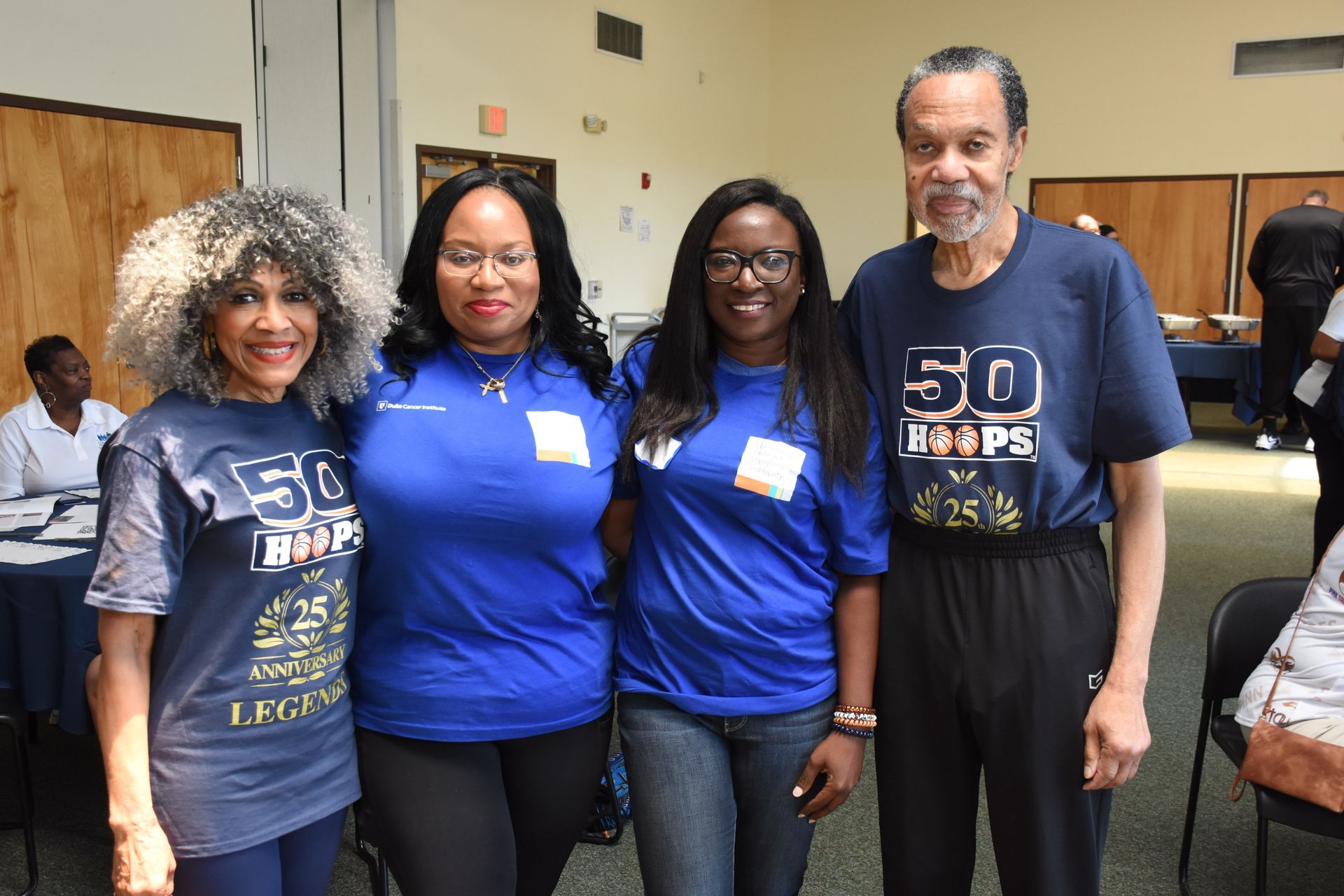 Four people in blue shirts pose indoors, one with gray curly hair. 