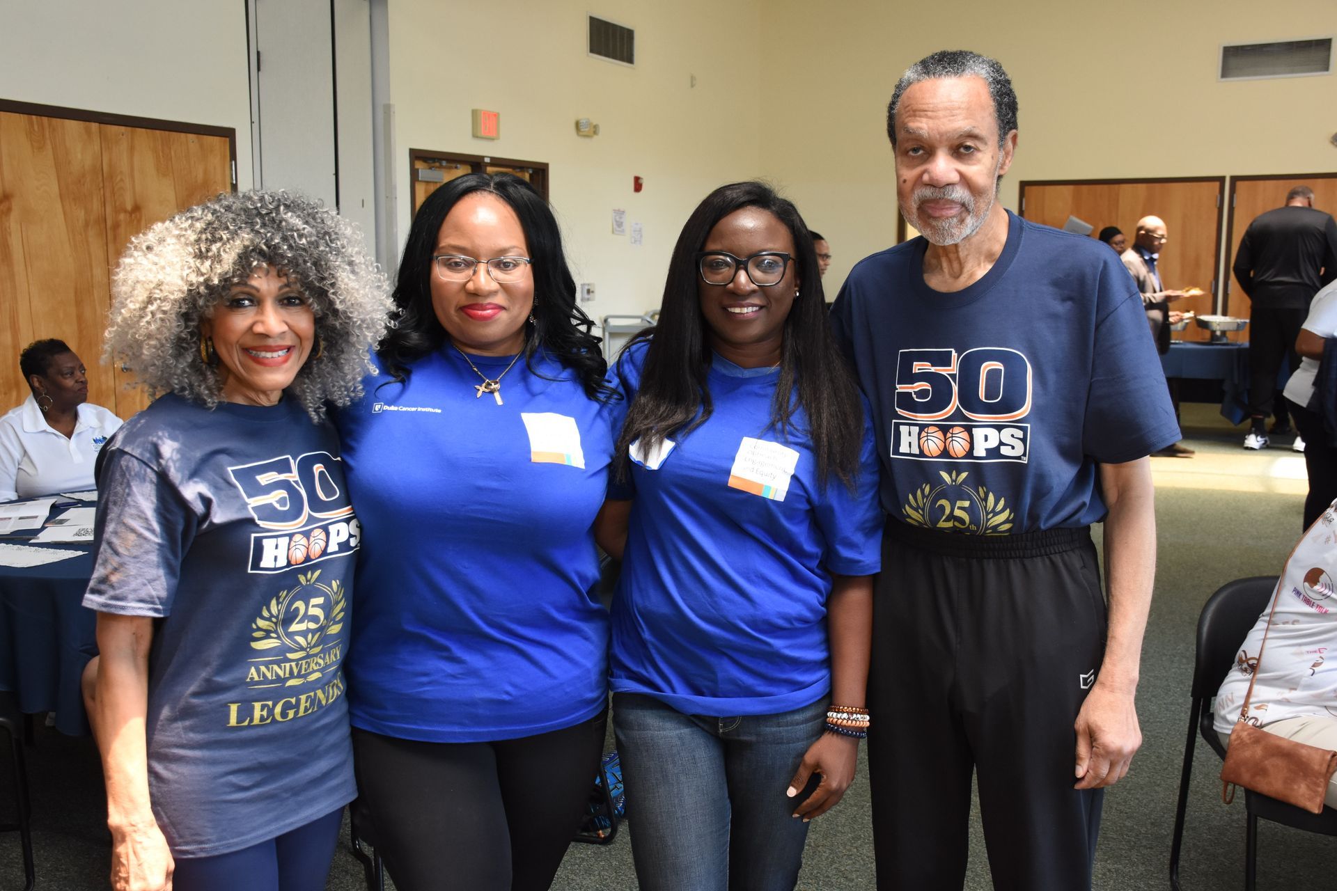 Four people in blue shirts pose indoors, smiling. 