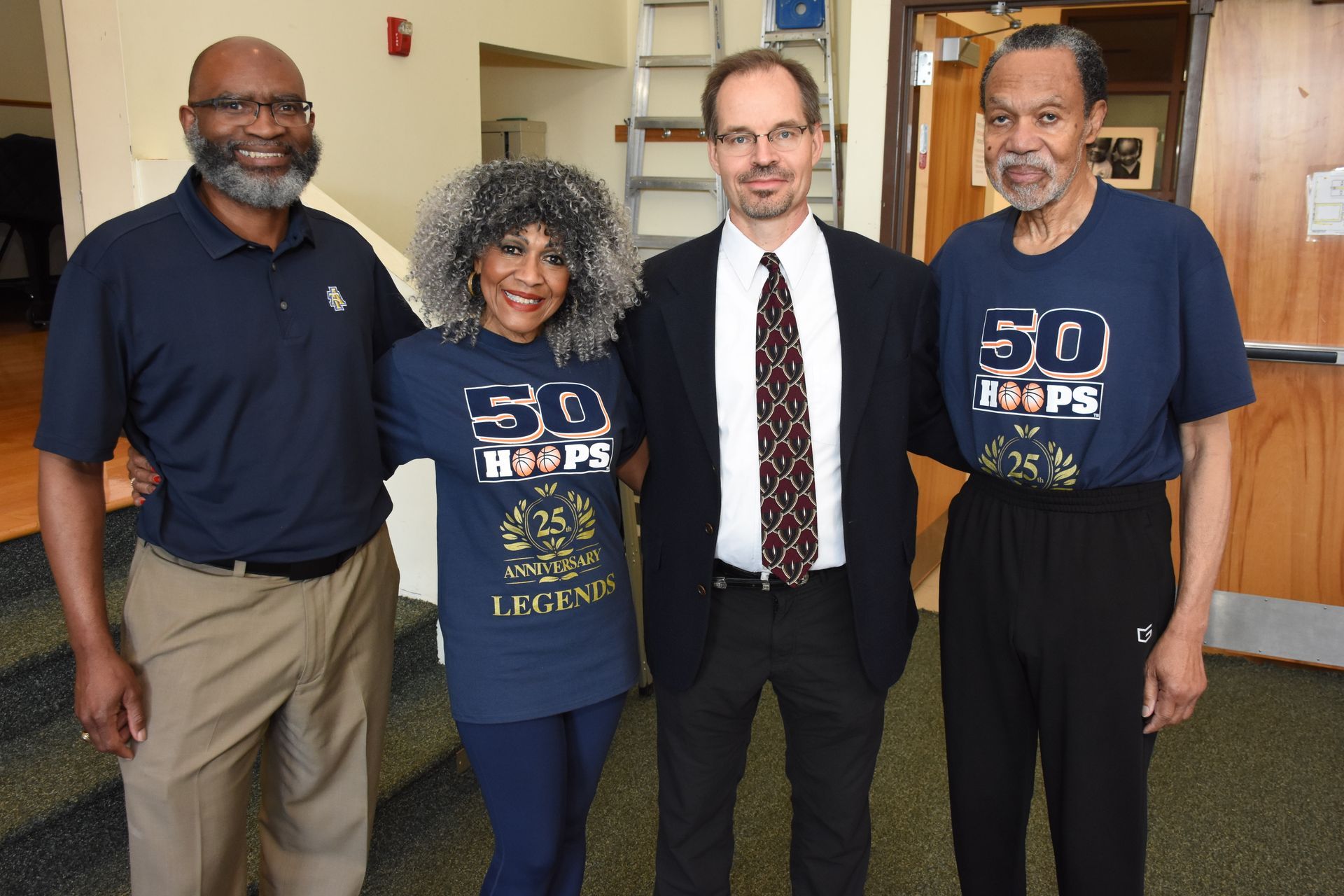 Four people pose indoors, two in navy 