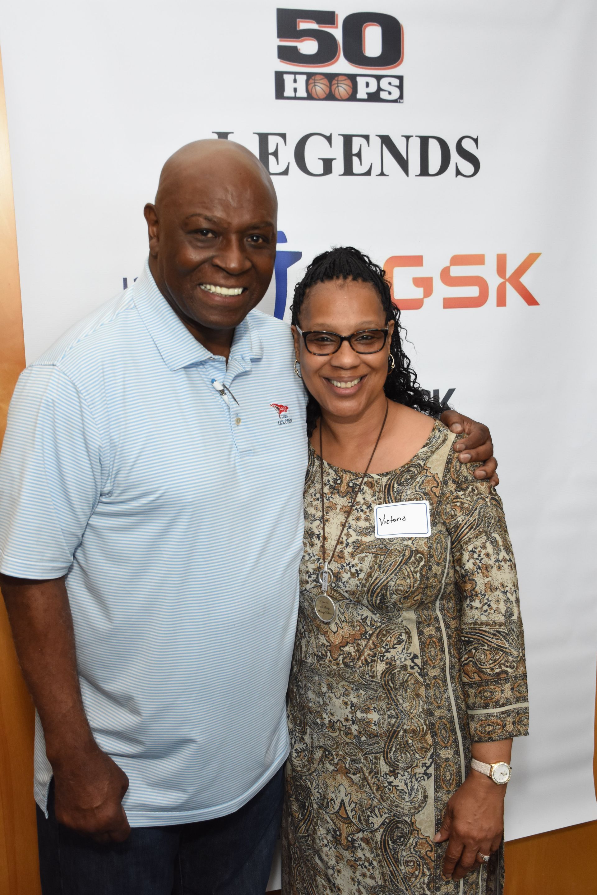 Man in blue shirt and woman in patterned dress pose together, smiling at an event with a 