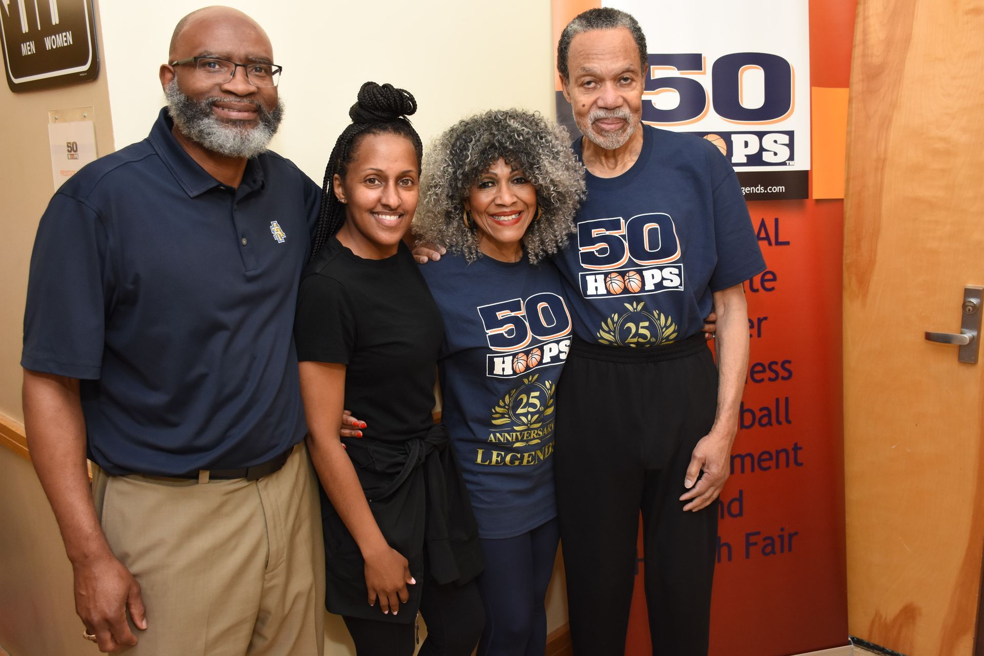 Four people pose for a photo. Two wear navy shirts with 