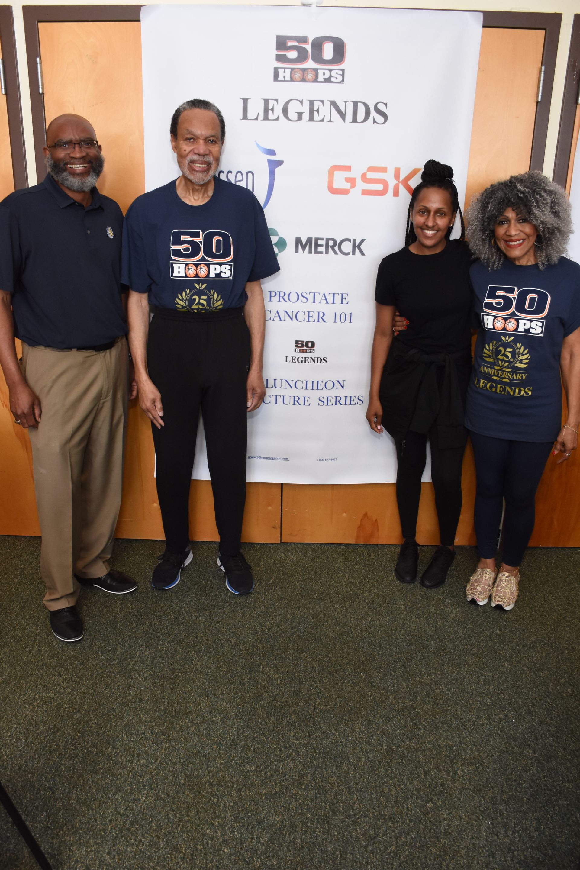 Four people stand in front of a banner; two men, two women. All are wearing matching shirts.