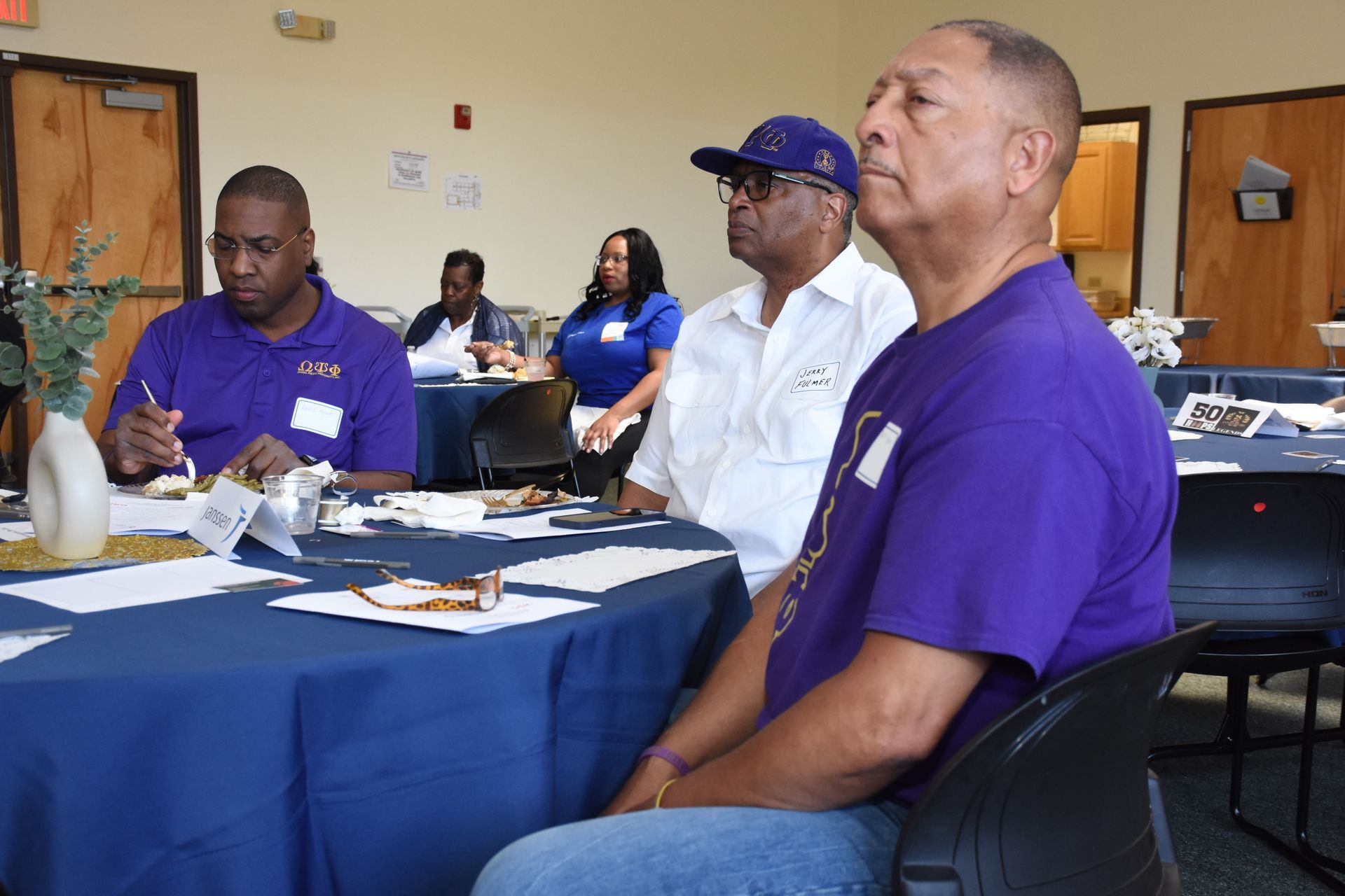 People in purple shirts sit at a table in a meeting.