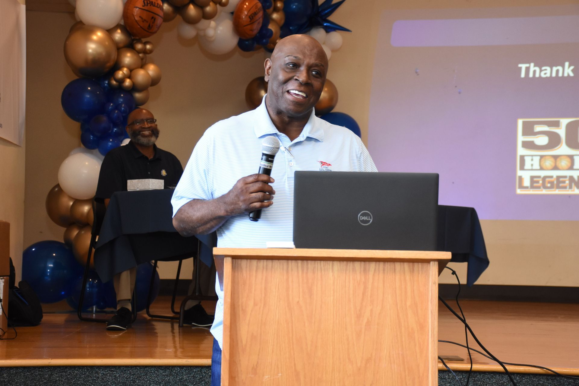 Man speaking at a podium, smiling, with a laptop. 