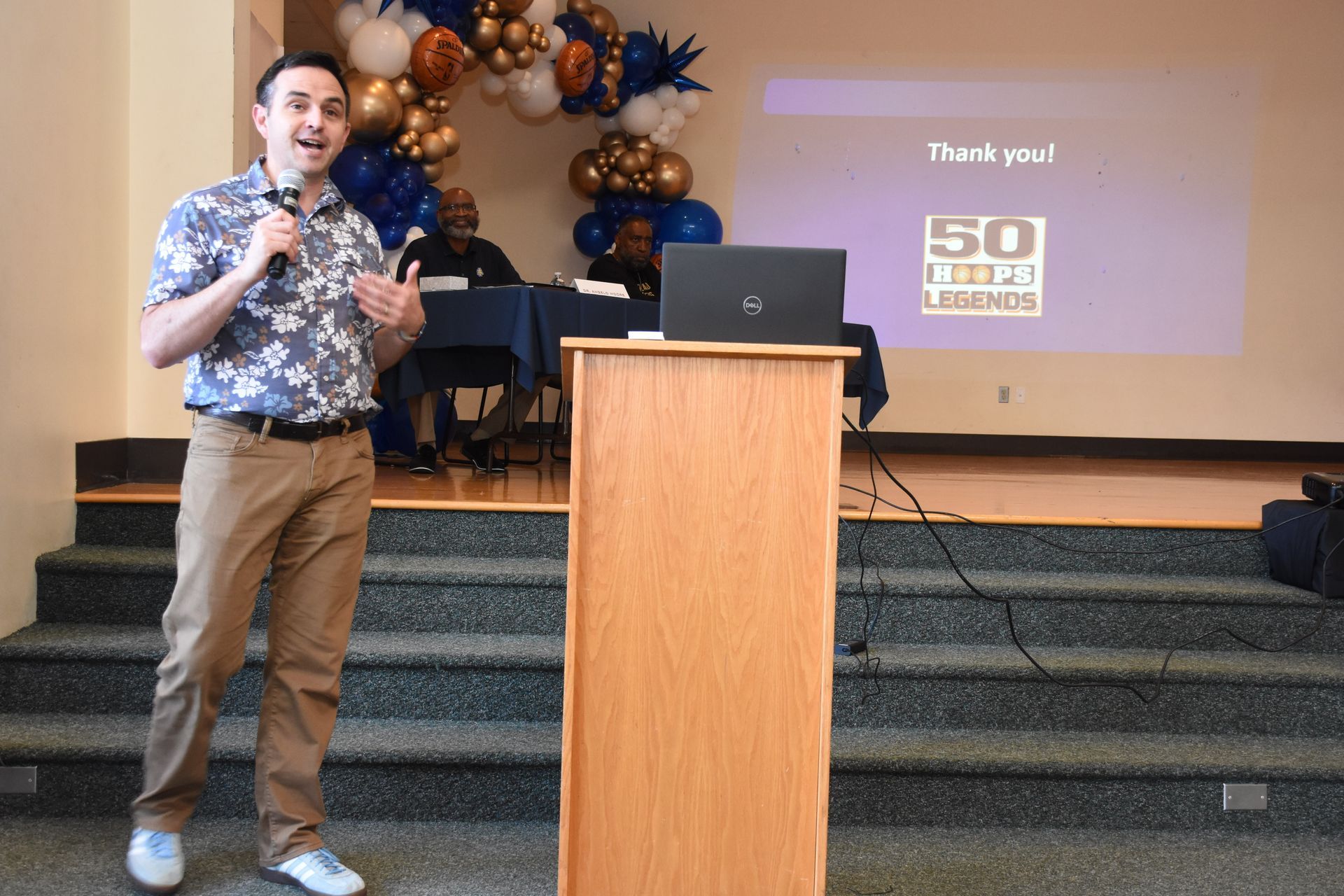 Man speaking at a podium, with a projection screen behind him that says 
