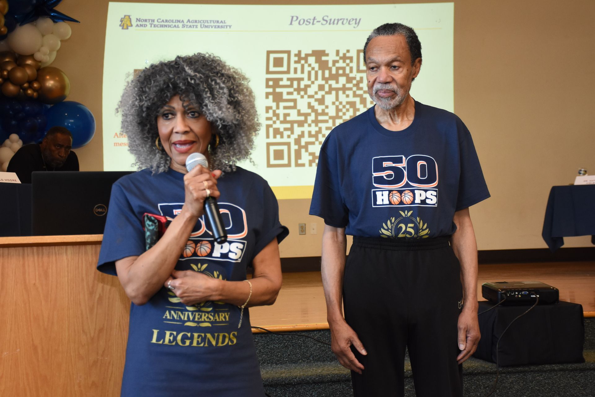Two people at a podium, each wearing a navy 