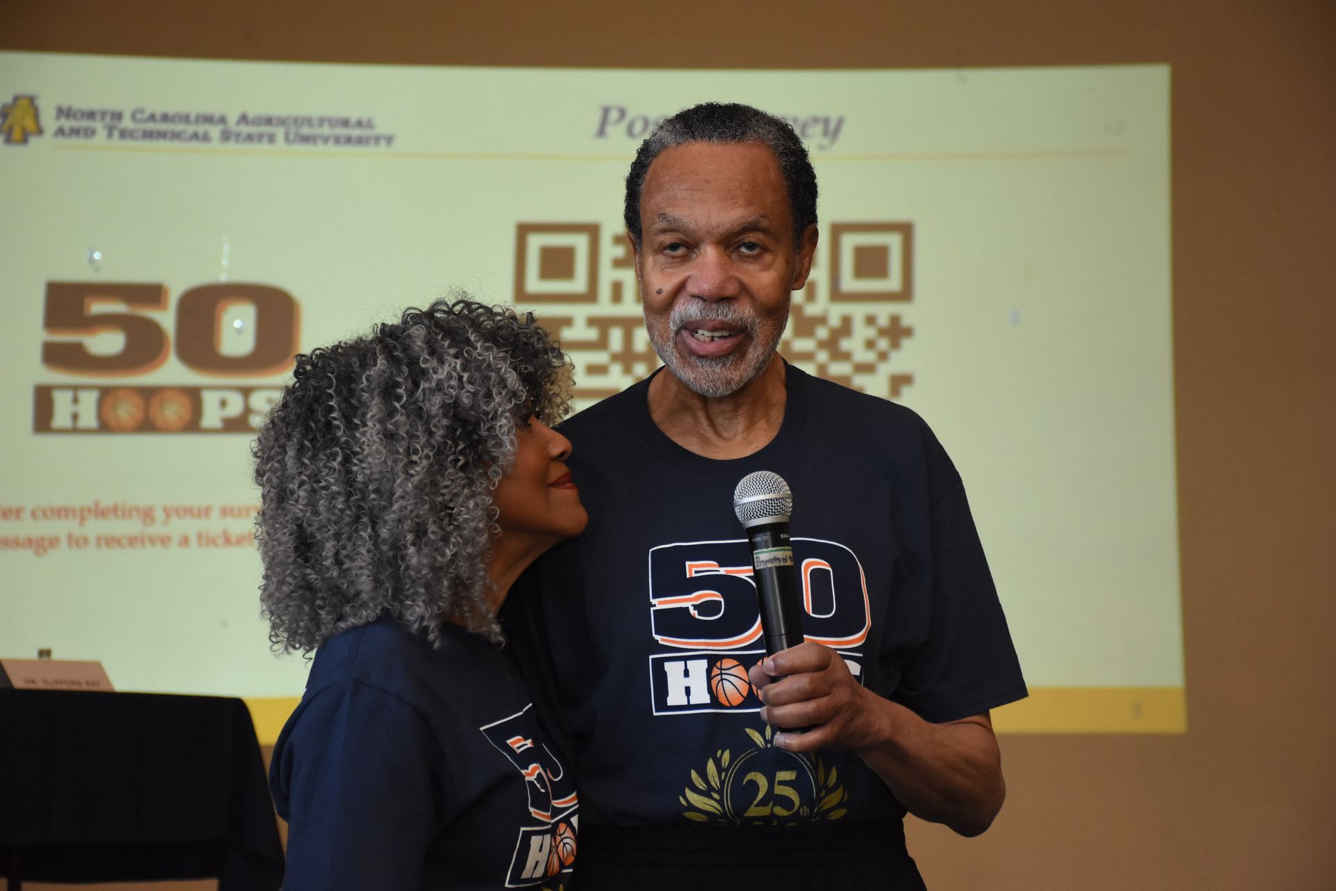 Man holding microphone with woman. Both wearing 