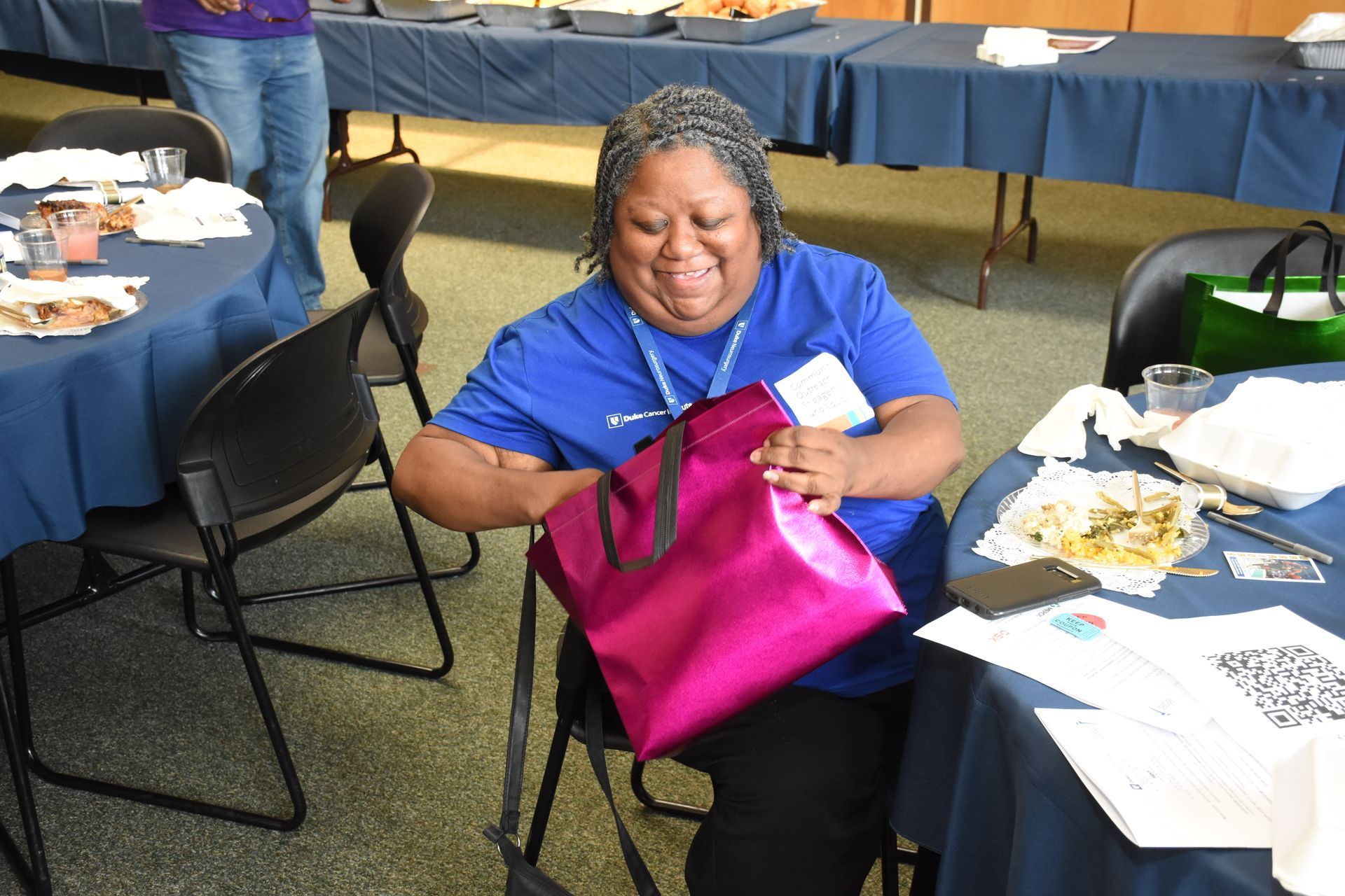 Woman opening a pink gift bag at a table in a room with blue tablecloths.