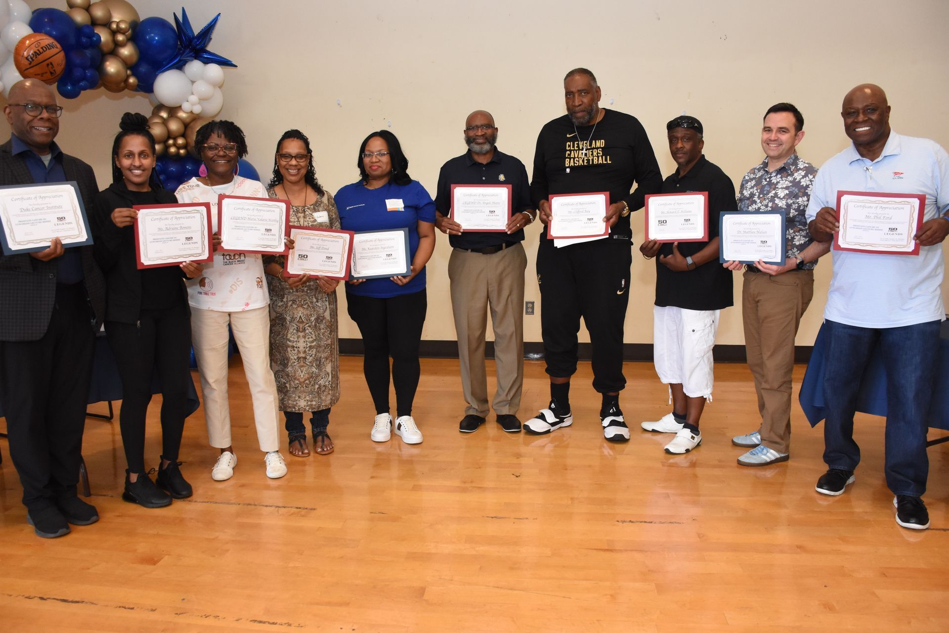 Group of people holding certificates, celebrating an event indoors with balloons.