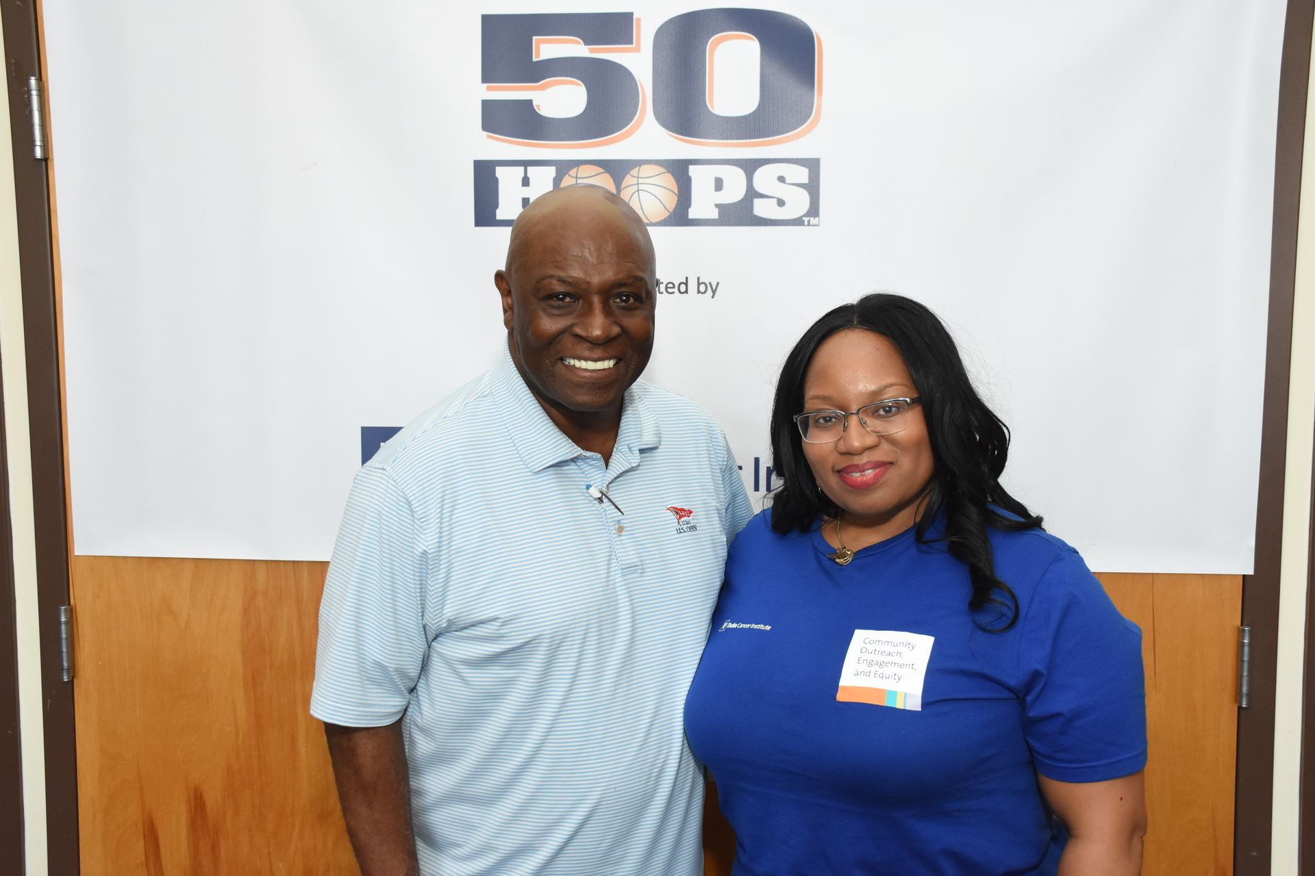 Two people stand smiling in front of a banner that reads 