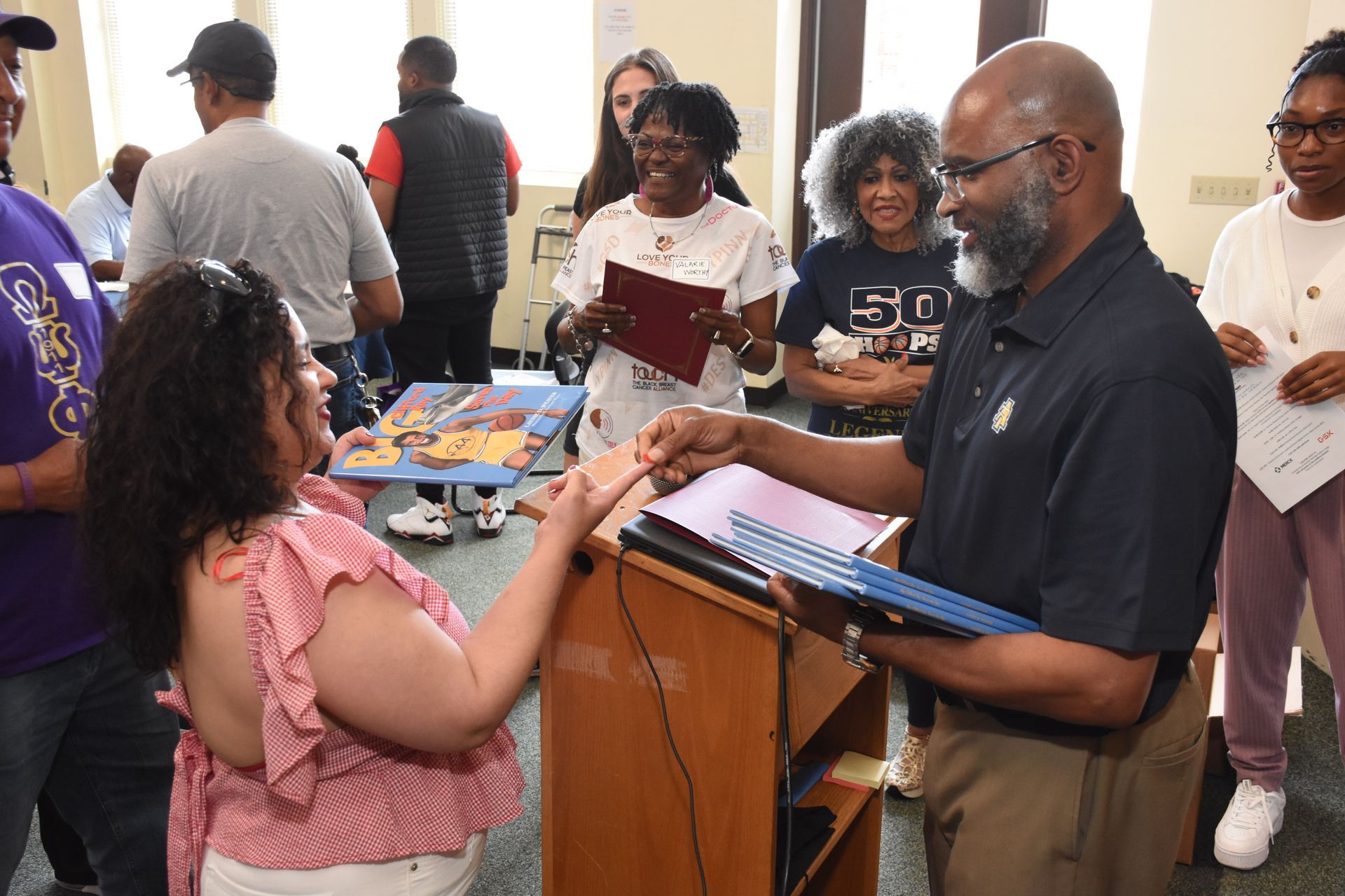 Man handing diploma to woman; people in background.