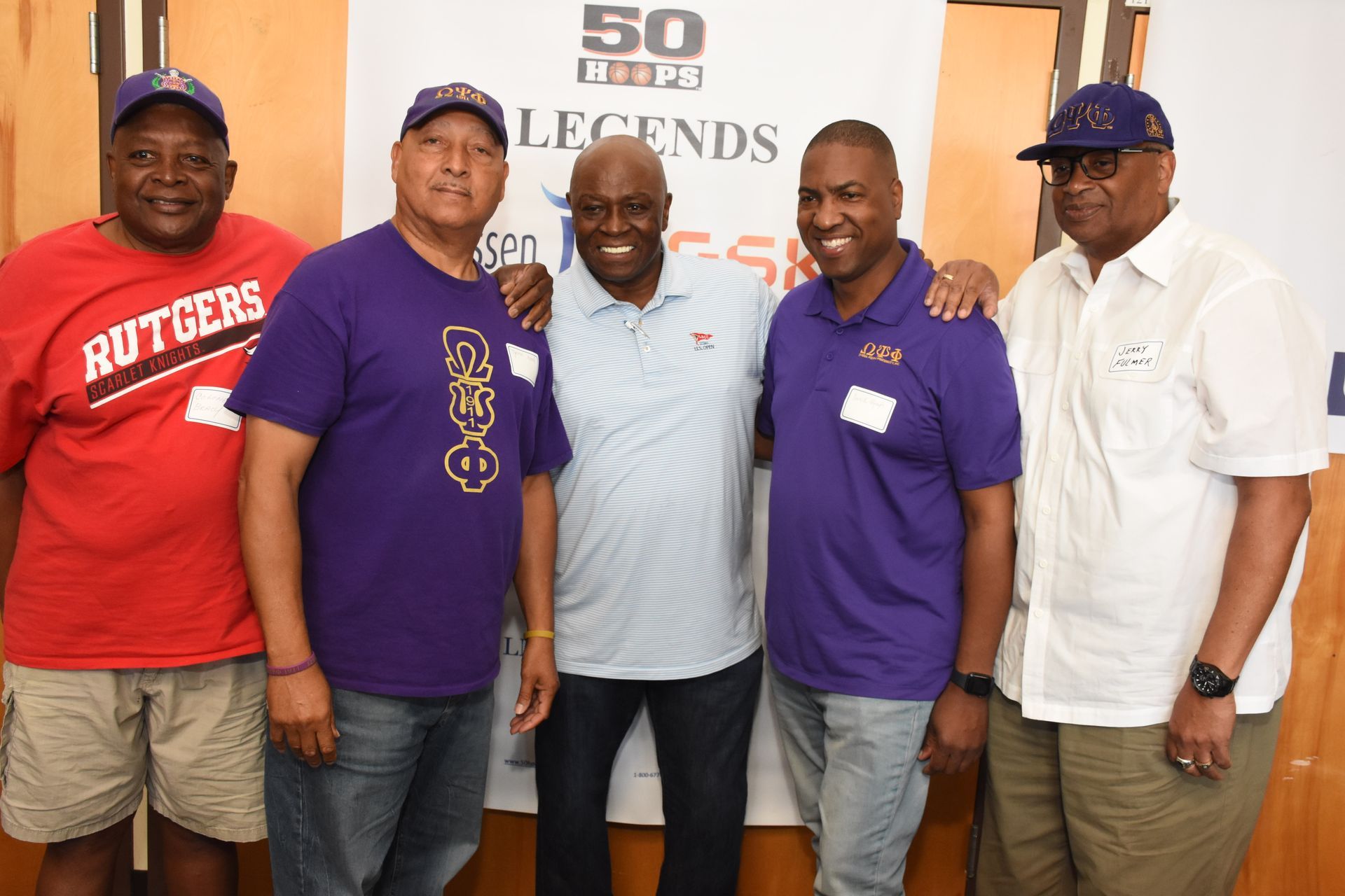 Five men posing together, some with arms around each other. One wears a Rutgers shirt, others purple shirts.