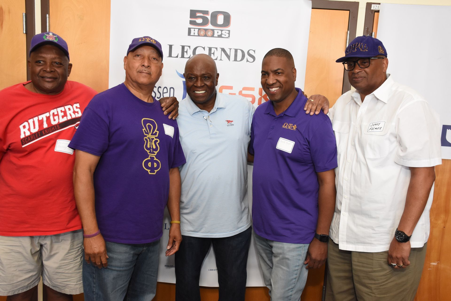 Five men pose for a photo in front of a banner. They are smiling.