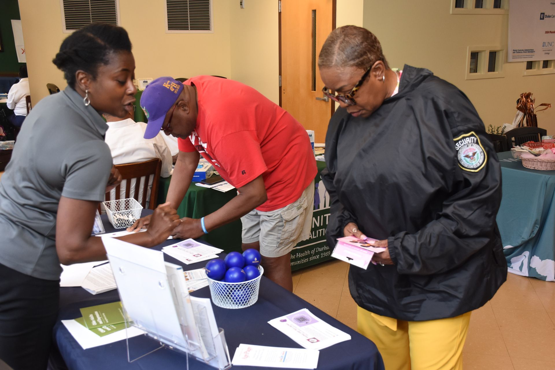 Woman assisting two people at a table, likely an informational event. Papers, blue balls, and a basket present.