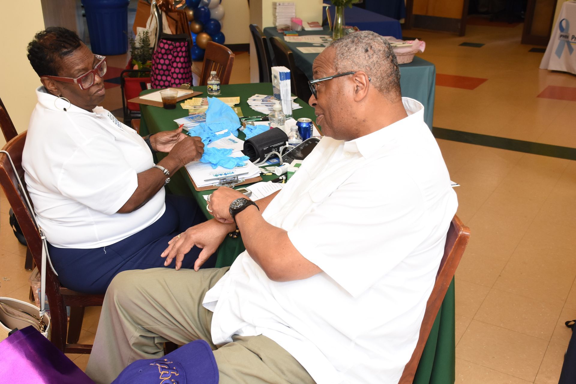 Two people sit at a table, both wearing white shirts. They are looking at items on the table.