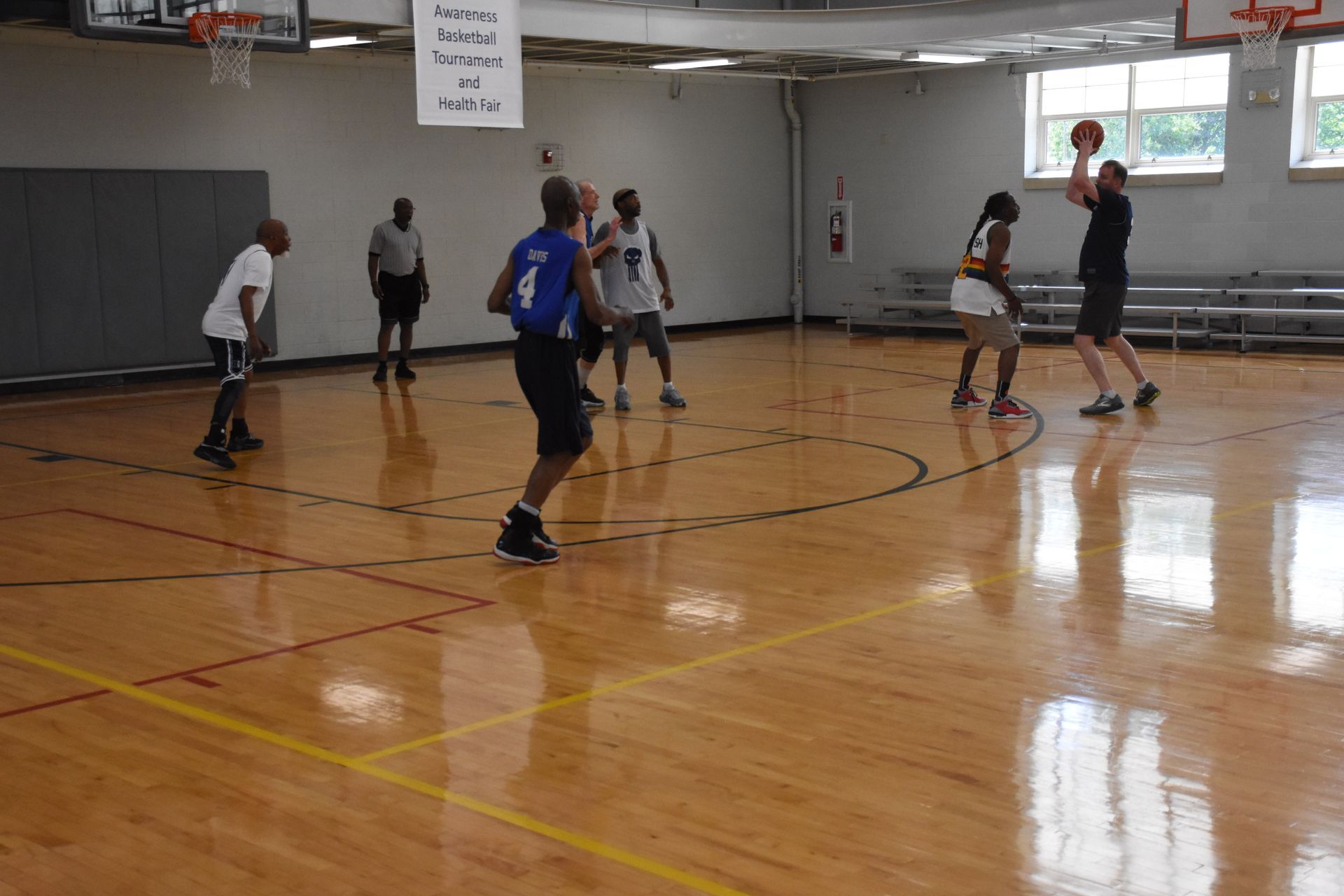People playing basketball in a gymnasium. One person shoots the ball.