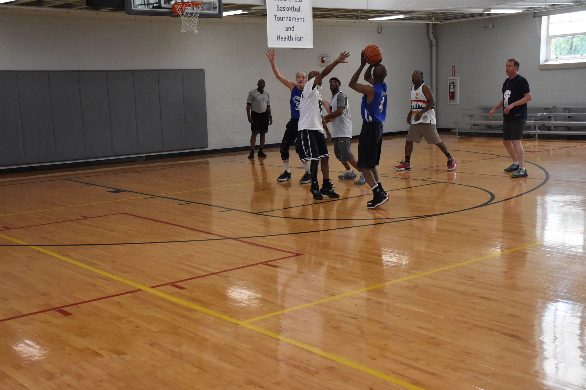 Basketball game in a gym: players shooting, defending, and running on a wood floor.