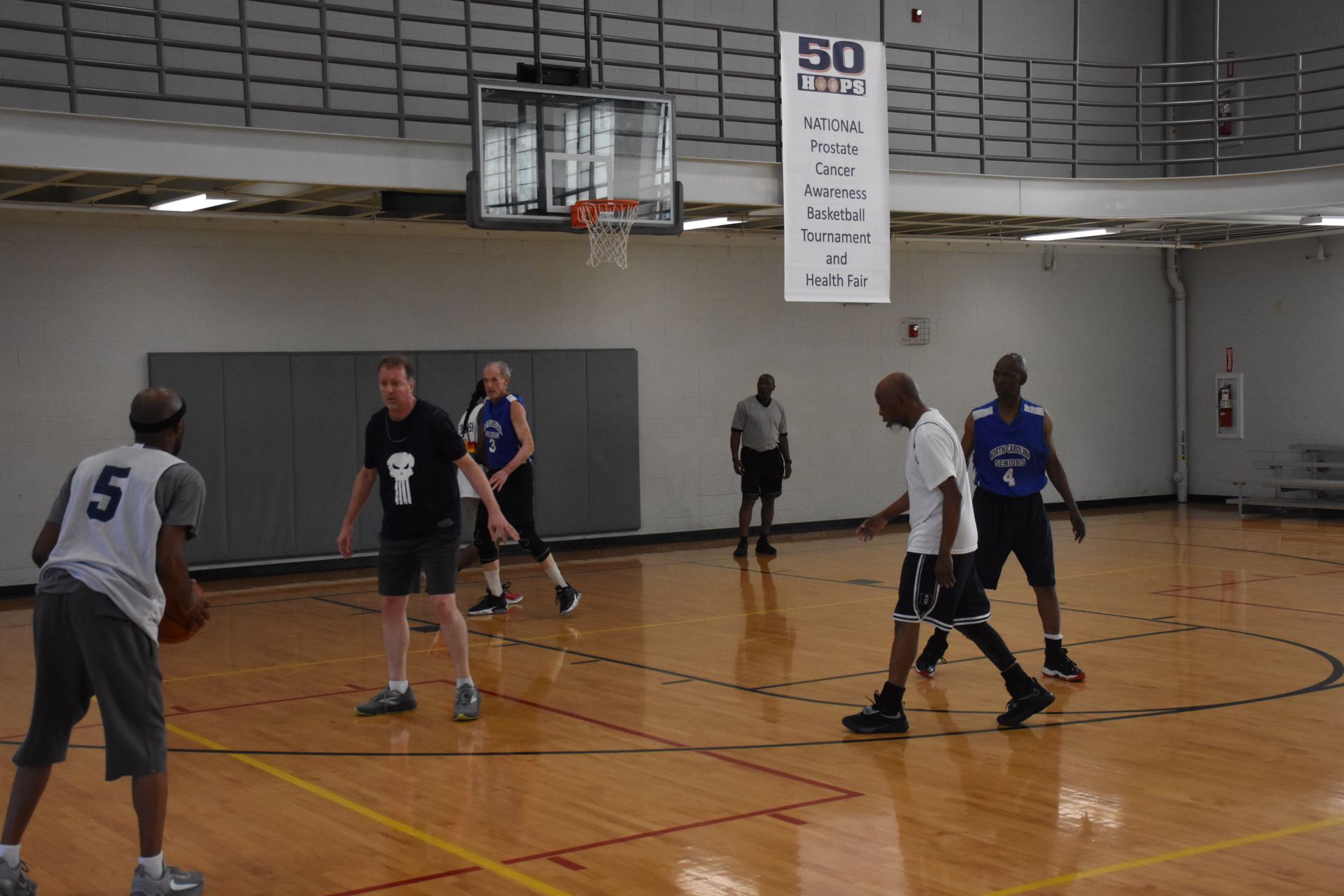 Basketball game in an indoor gym. Players in jerseys dribble and defend on a wooden court.