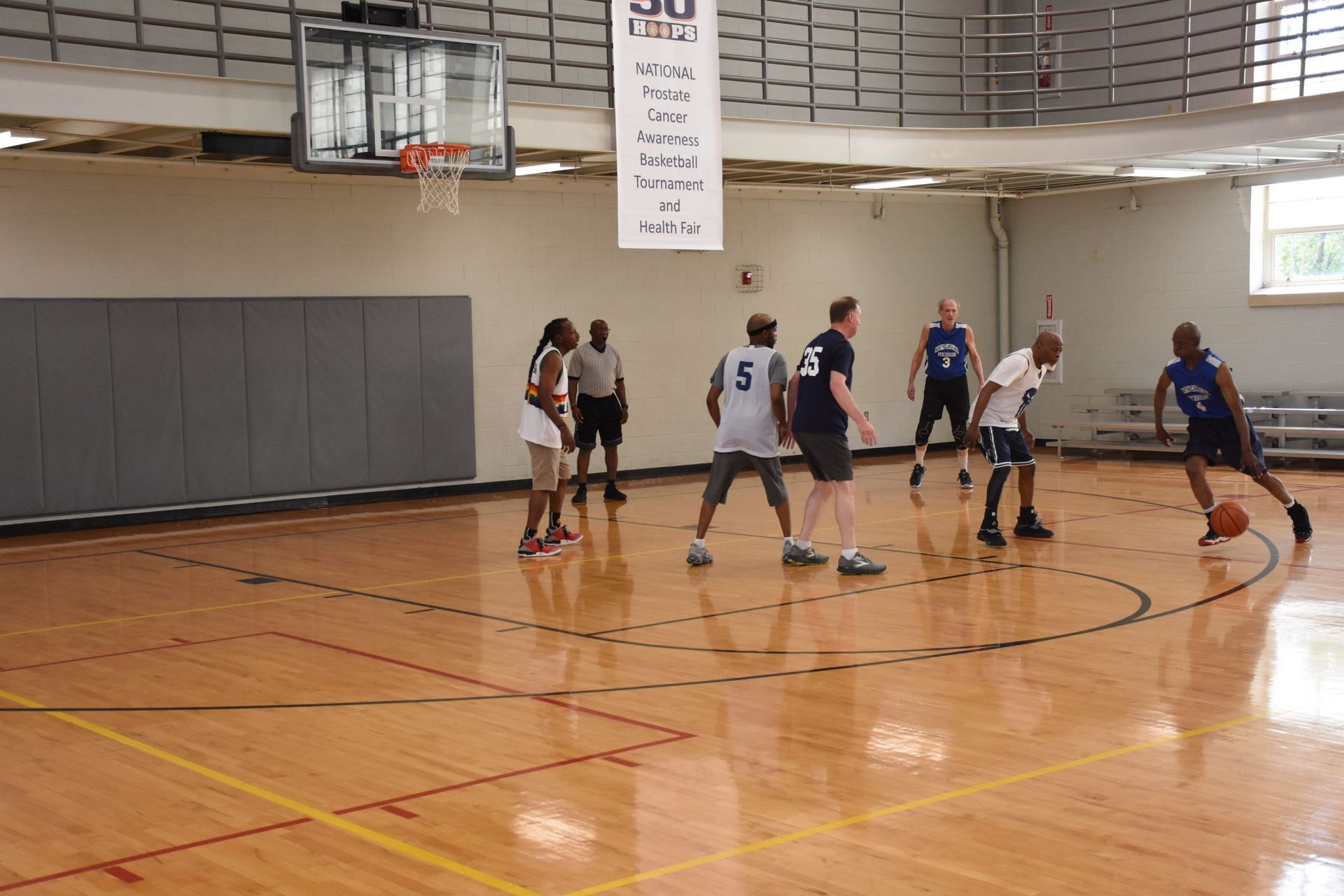 Basketball game in progress in a gym. Players dribble, pass, and defend the ball near the court's center.