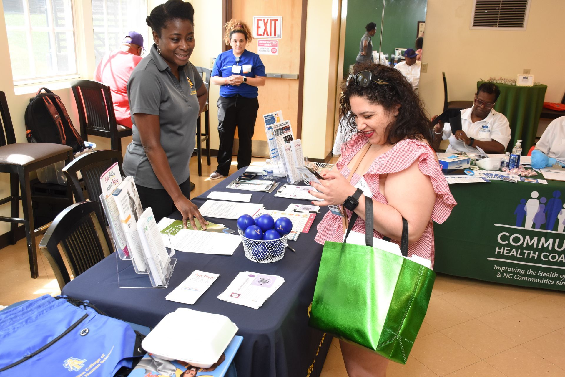 Woman looking at phone at a table with a staff member. Promotional table at community event.