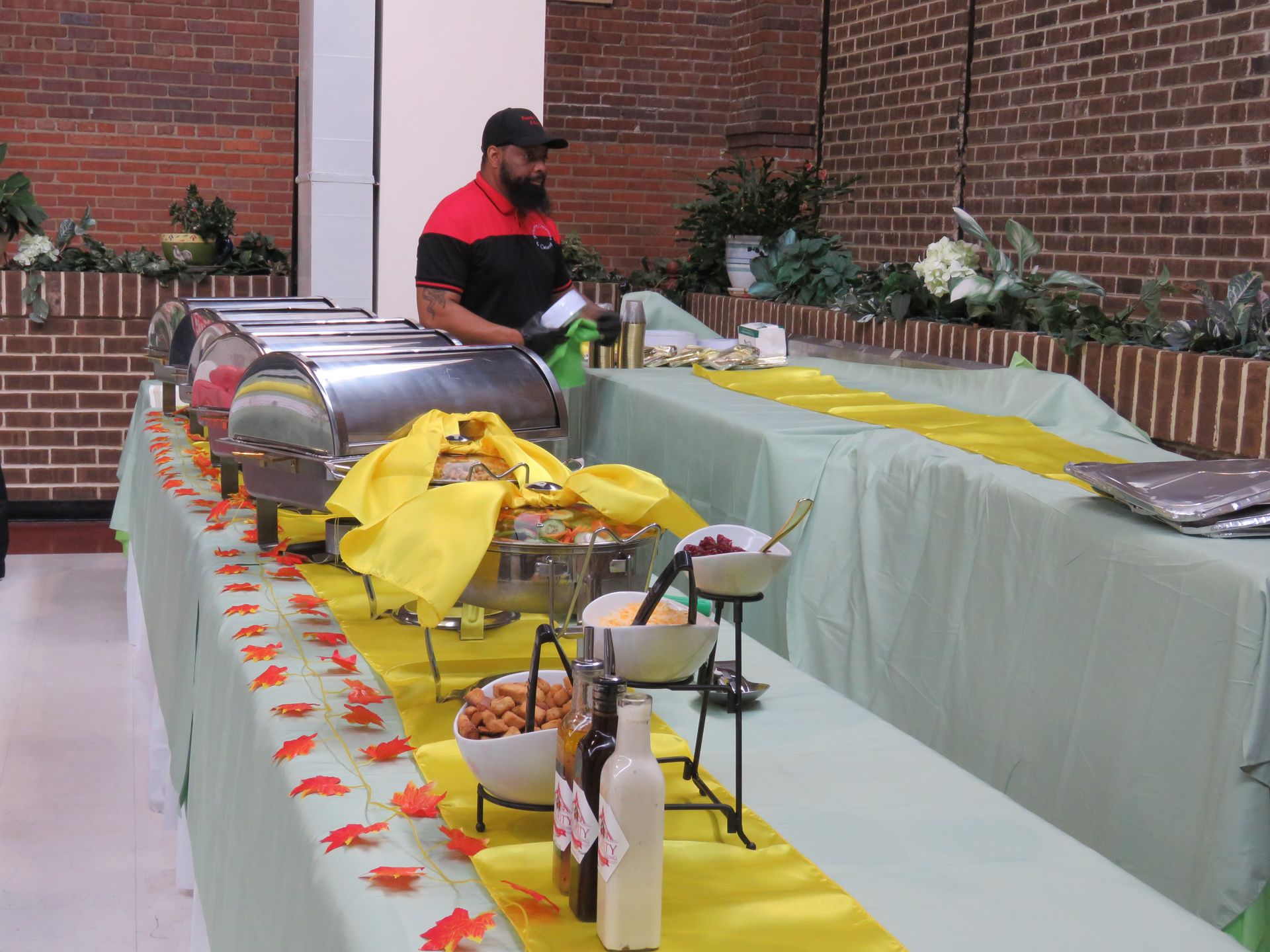 Buffet with food and server; yellow table runners and decor in brick-walled room.